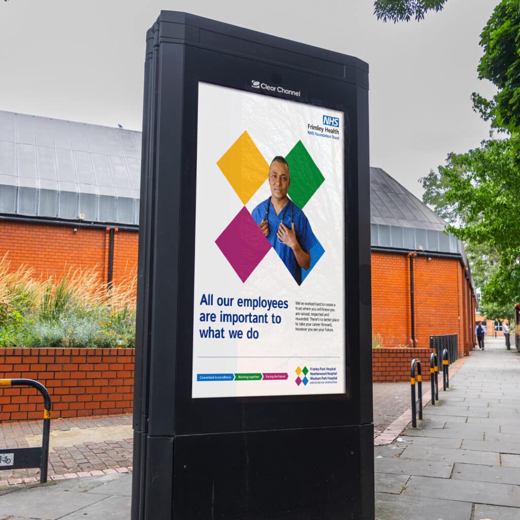Outdoor digital screen displaying a Frimley Health recruitment campaign poster featuring a staff member with the message “All our employees are important to what we do”. The design uses a distinctive diamond graphic in NHS brand colours to communicate values and inclusivity.