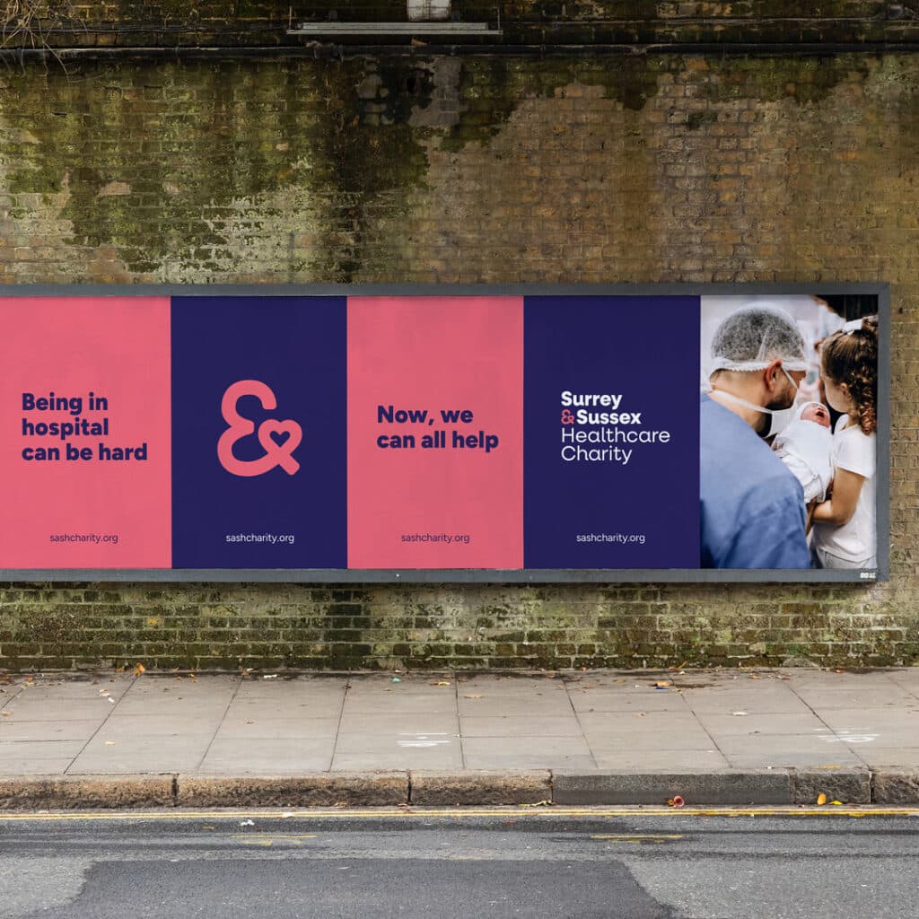 Large roadside billboard featuring a campaign for Surrey & Sussex Healthcare Charity. Bold panels of colour carry simple, empathetic messaging—‘Being in hospital can be hard’ and ‘Now, we can all help’—supported by the charity’s ampersand heart symbol and a warm photograph of a parent and baby with a healthcare worker