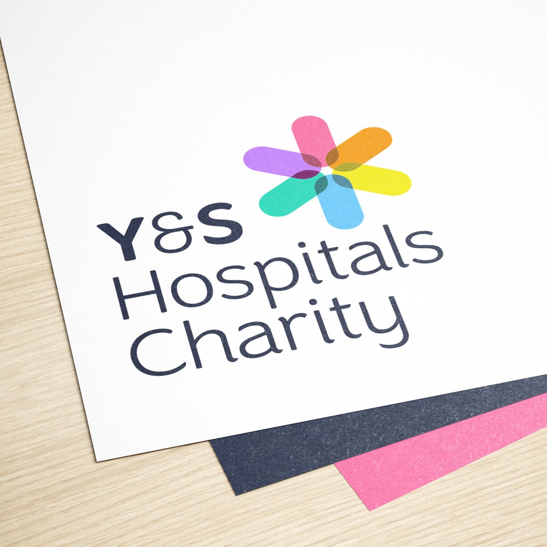 Close-up of the York & Scarborough Hospitals Charity logo on white paper, with a colourful abstract flower symbol and clean, accessible typography.