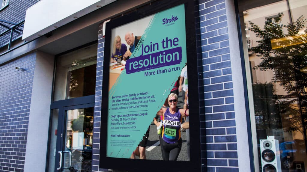 Digital poster on a city street promoting the Stroke Association's Resolution Run campaign, featuring the slogan "Join the resolution – More than a run," with images of stroke survivors and participants, including a smiling runner wearing a purple Stroke Association vest and race number.