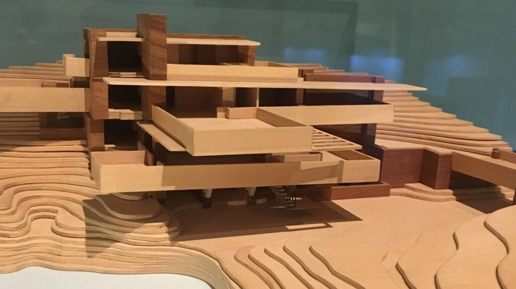 Architectural model made of wood showing a layered, geometric design with cantilevered sections and terraces.