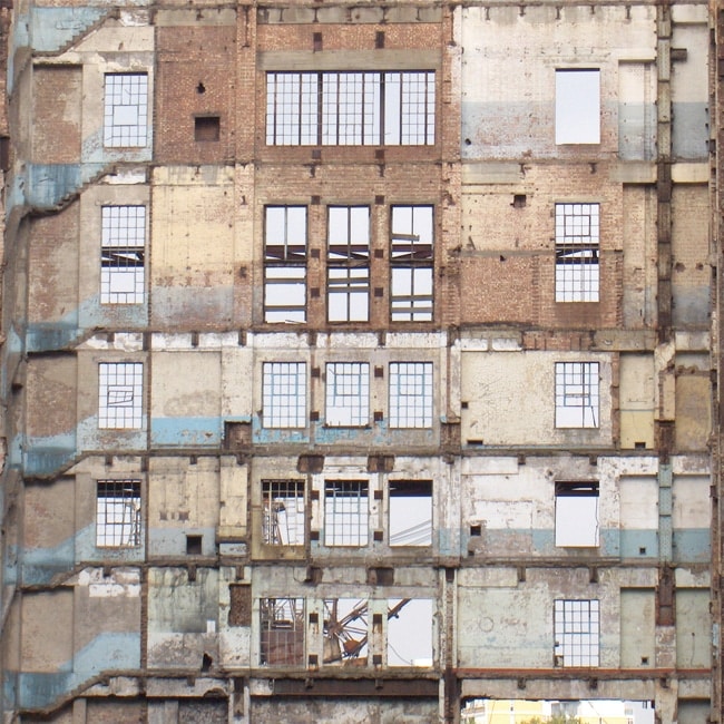 Exposed facade of a derelict industrial building with visible window grids.