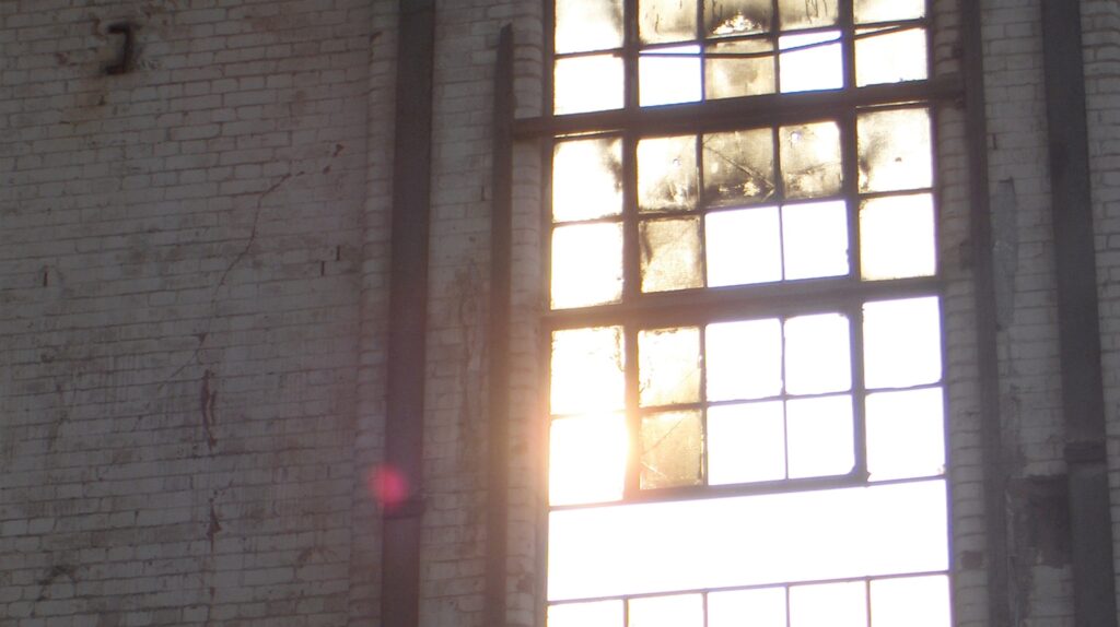 Sunlight pouring through a large industrial window in a brick wall.