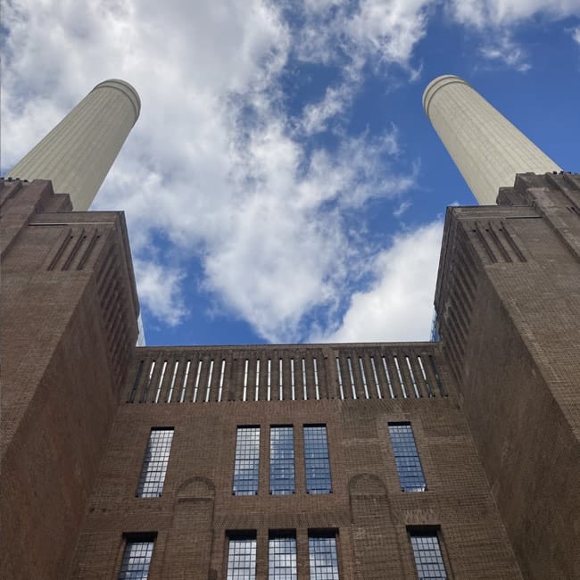 Upward view of Battersea Power Station chimneys against a blue sky.