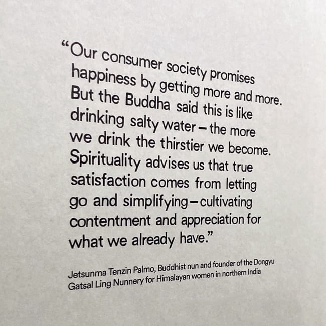 Inspirational quote on a gallery wall about consumerism and spiritual contentment, attributed to Jetsunma Tenzin Palmo.