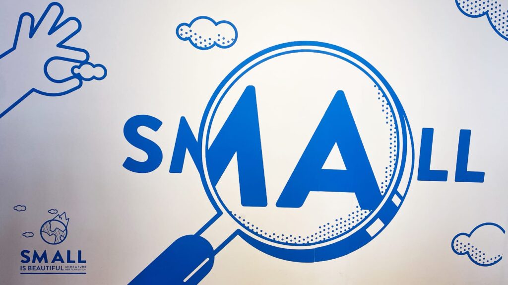 Exhibition wall artwork reading 'SMALL IS BEAUTIFUL' with magnifying glass design.