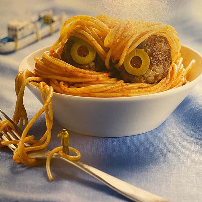 Playful spaghetti and meatball dish made to resemble a face with olive eyes.