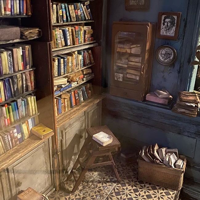 Miniature model of a vintage bookshop with worn shelves and stacked books.