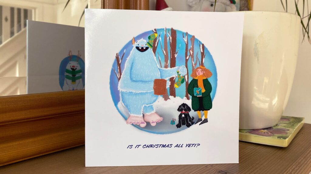 Illustrated Christmas card featuring a blue yeti giving gifts to a girl and a dog in a snowy forest, with the caption 'Is it Christmas all Yeti?'