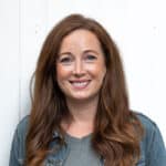 Portrait of Laura Corbett, Creative Director at Ave Design, smiling in front of a white panelled wall.