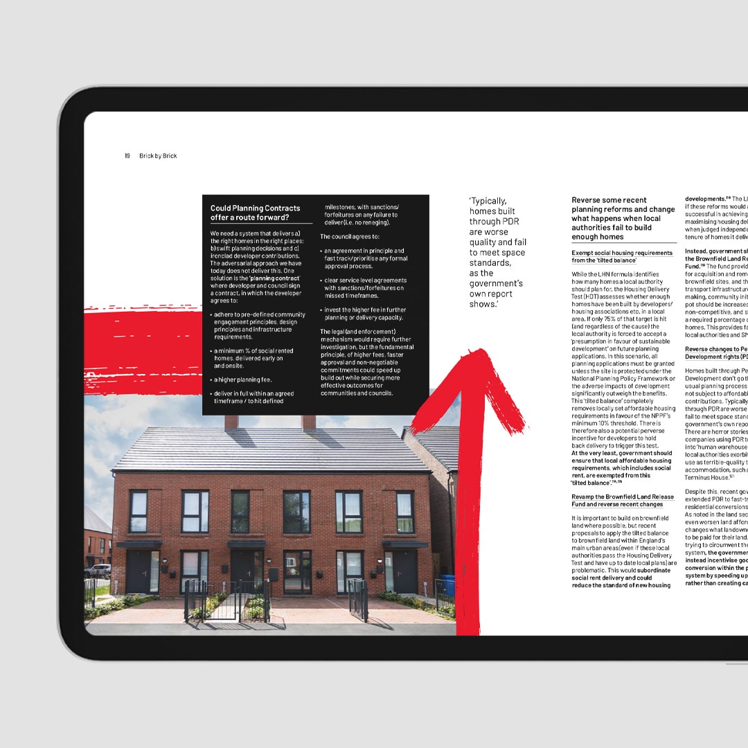 Tablet screen displaying a digital spread of Shelter’s housing report, featuring new-build homes, detailed policy text, and a bold red painted arrow drawing attention to key content.