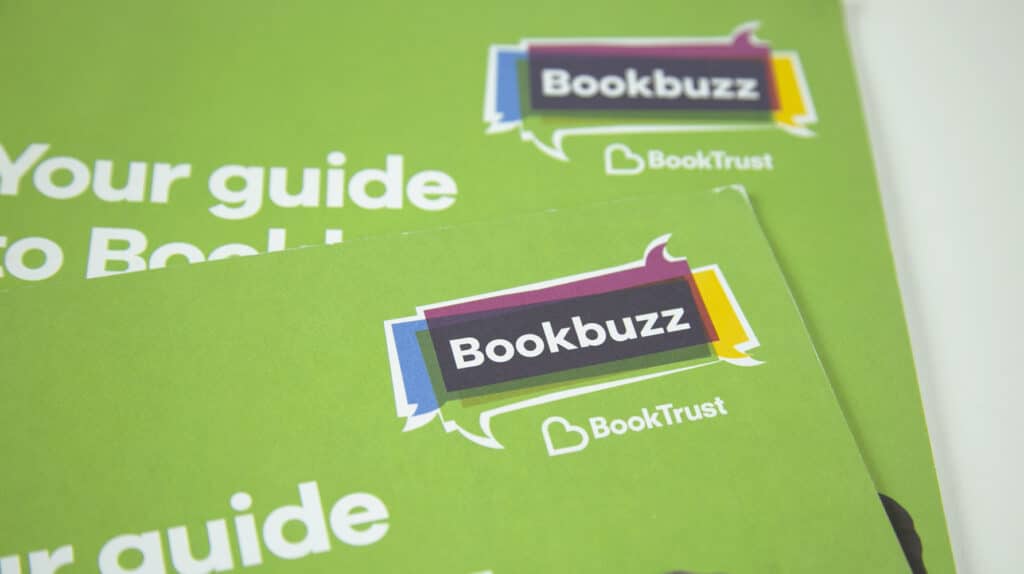 Close-up of two overlapping green Bookbuzz guides by BookTrust, featuring a colourful speech bubble logo and bold white typography.